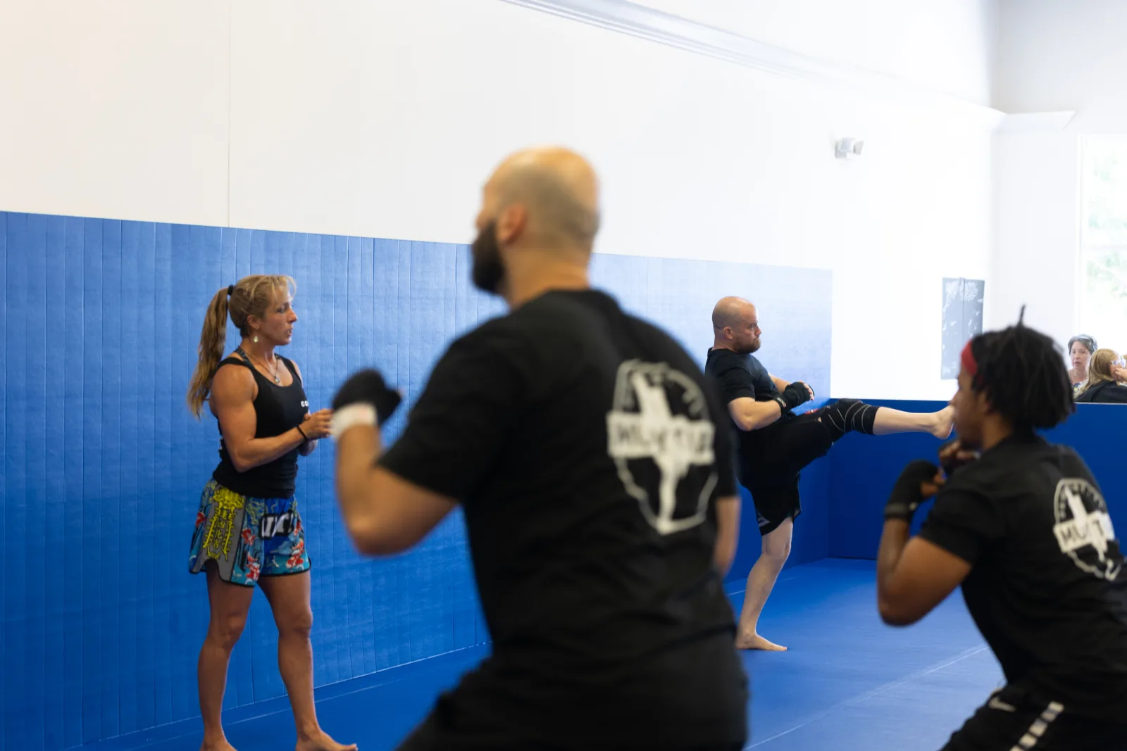 Adult Gracie Barra Davenport student throwing a high kick during Muay Thai class while the coach watches